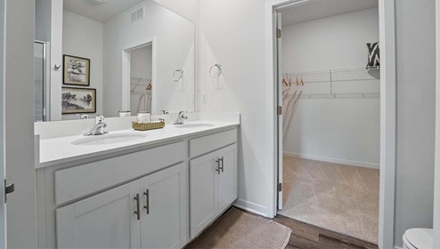 Bathroom with double sink vanity, standing glass door shower, and entryway to the walk in closet