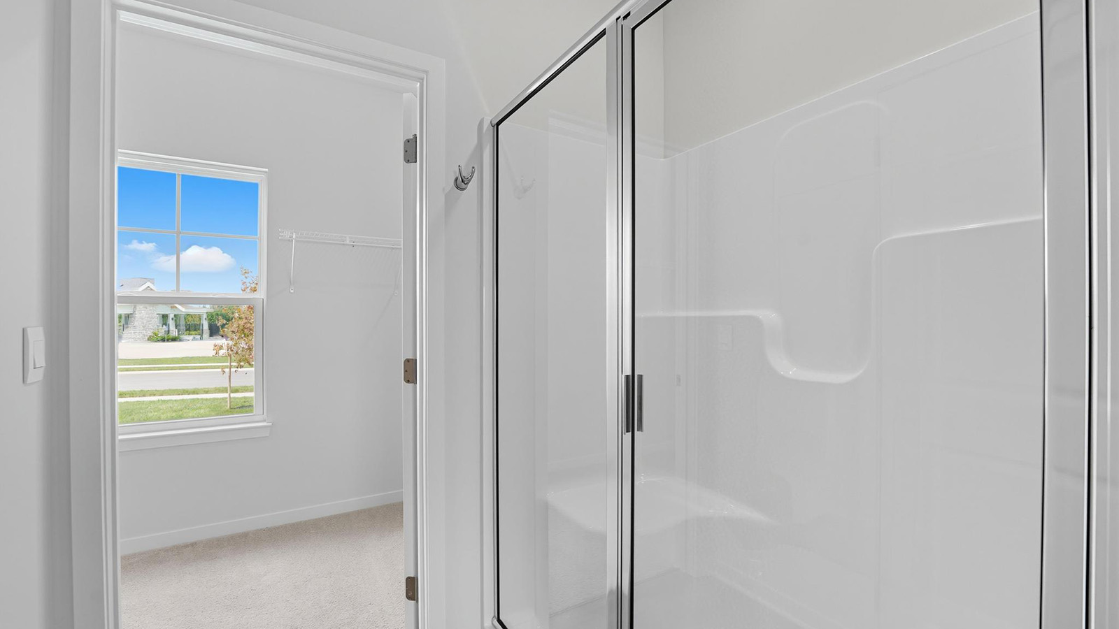 Primary bathroom with double sink vanity, standing glass door shower, and entryway to the walk in closet