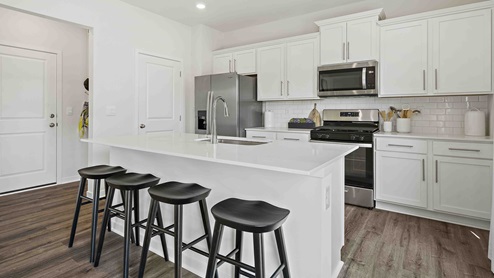 Kitchen and island with white cabinets and stainless steel appliances. New Homes in Kansas City, Missouri