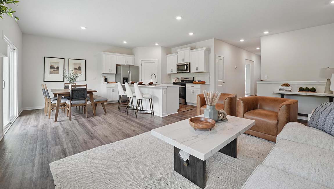 Living room with electric fireplace and two large windows, beside kitchen and dining area.