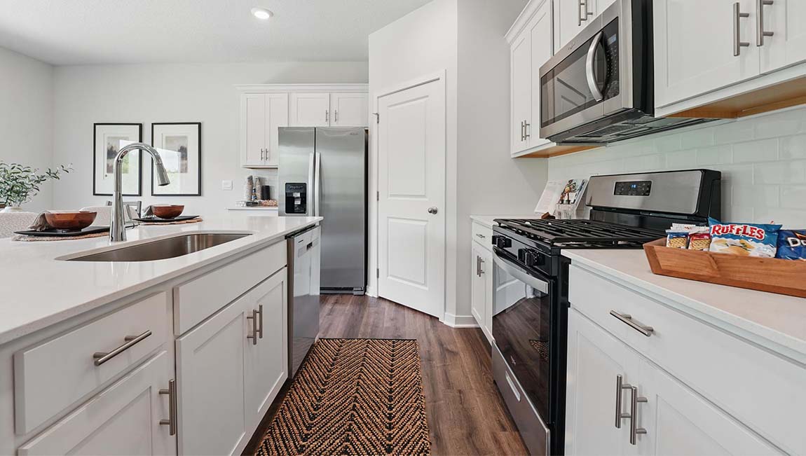 Kitchen and island with white cabinets, subway tile backsplash and stainless steel appliances.