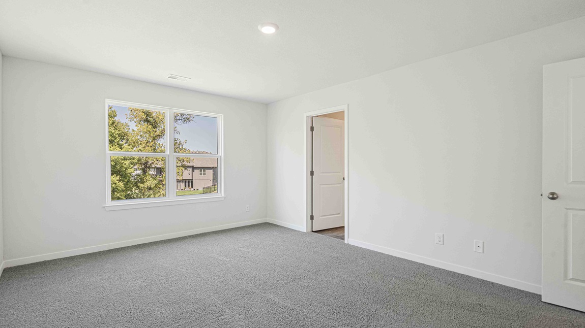 Carpeted primary bedroom with large window.