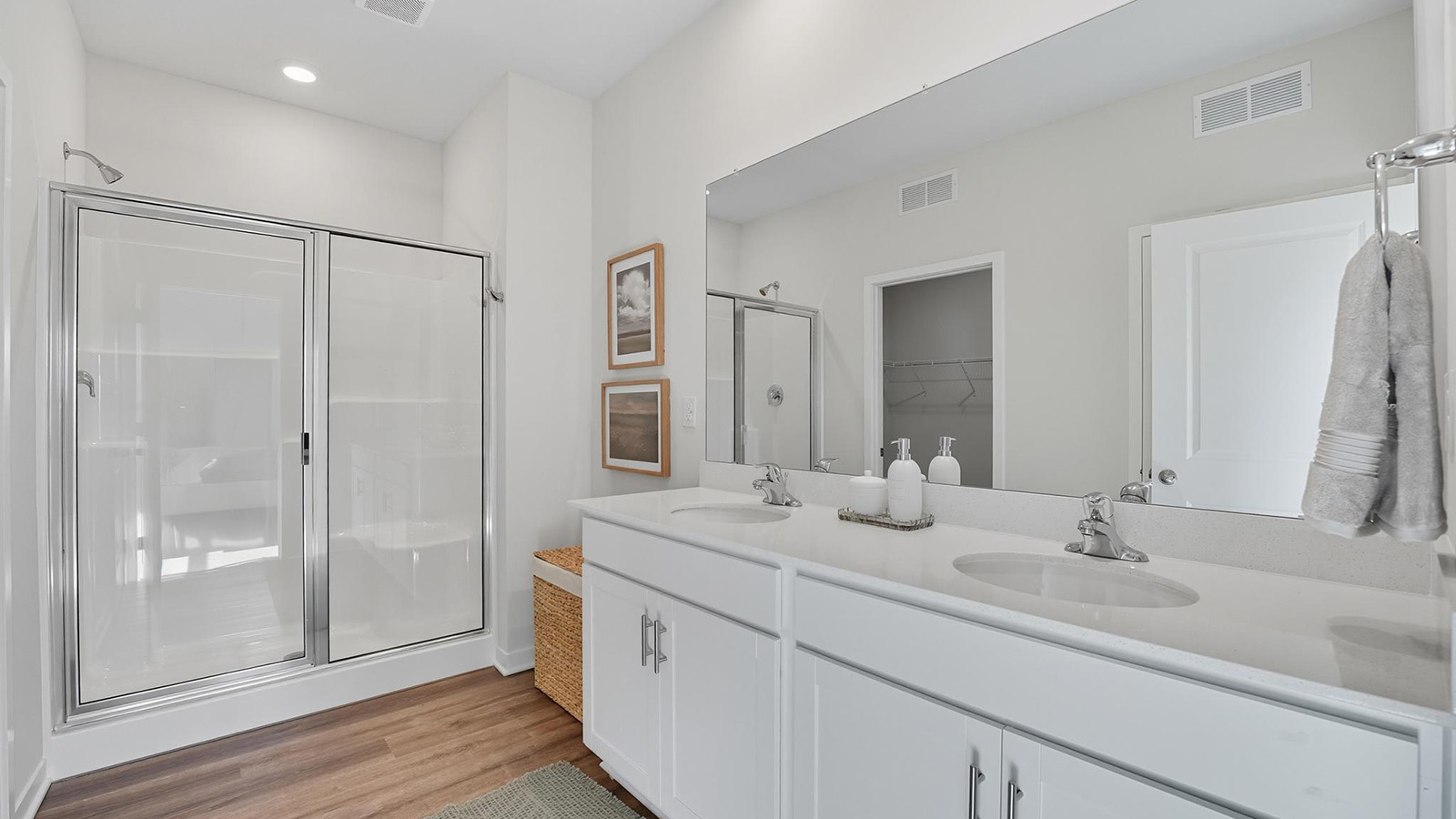 Bathroom with double sink vanity, standing glass door shower, and entryway to the walk in closet