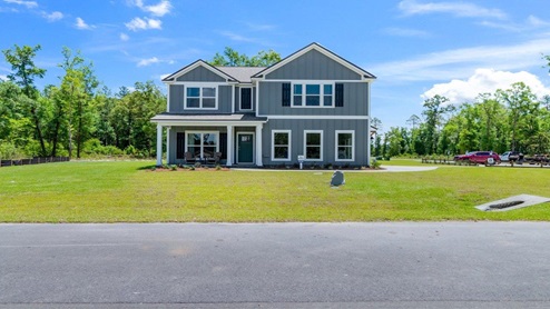 Exterior of the model home painted grey with black shutters on a large lot