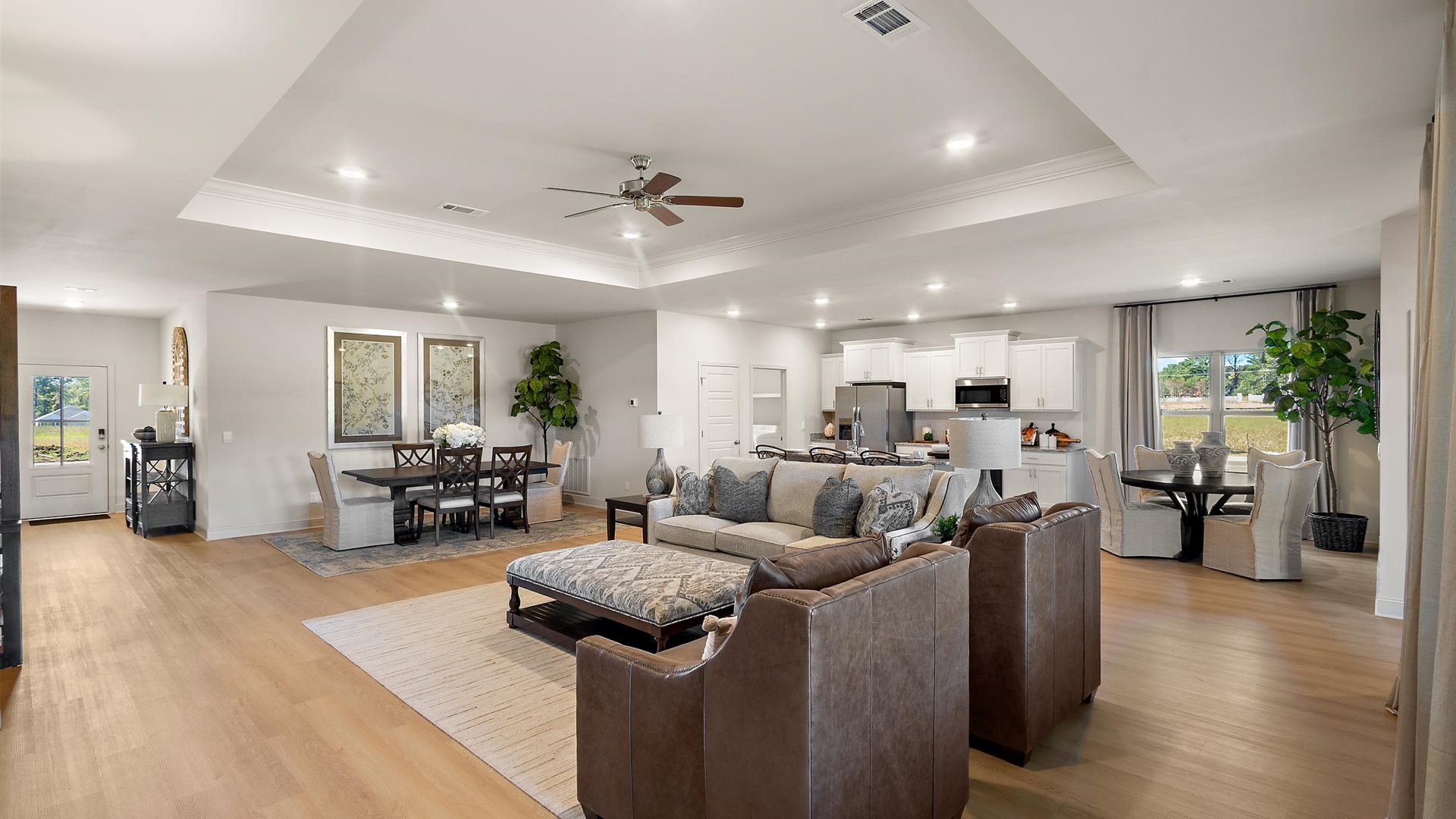 A spacious open floor plan living room, large windows, hardwood floors, and tray ceilings.