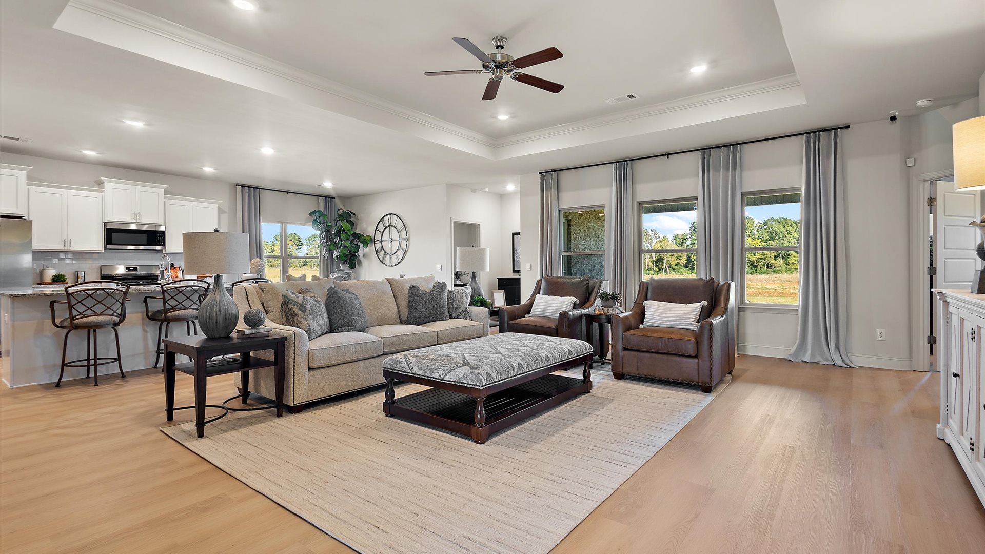 A spacious open floor plan living room, large windows, hardwood floors, and tray ceilings.