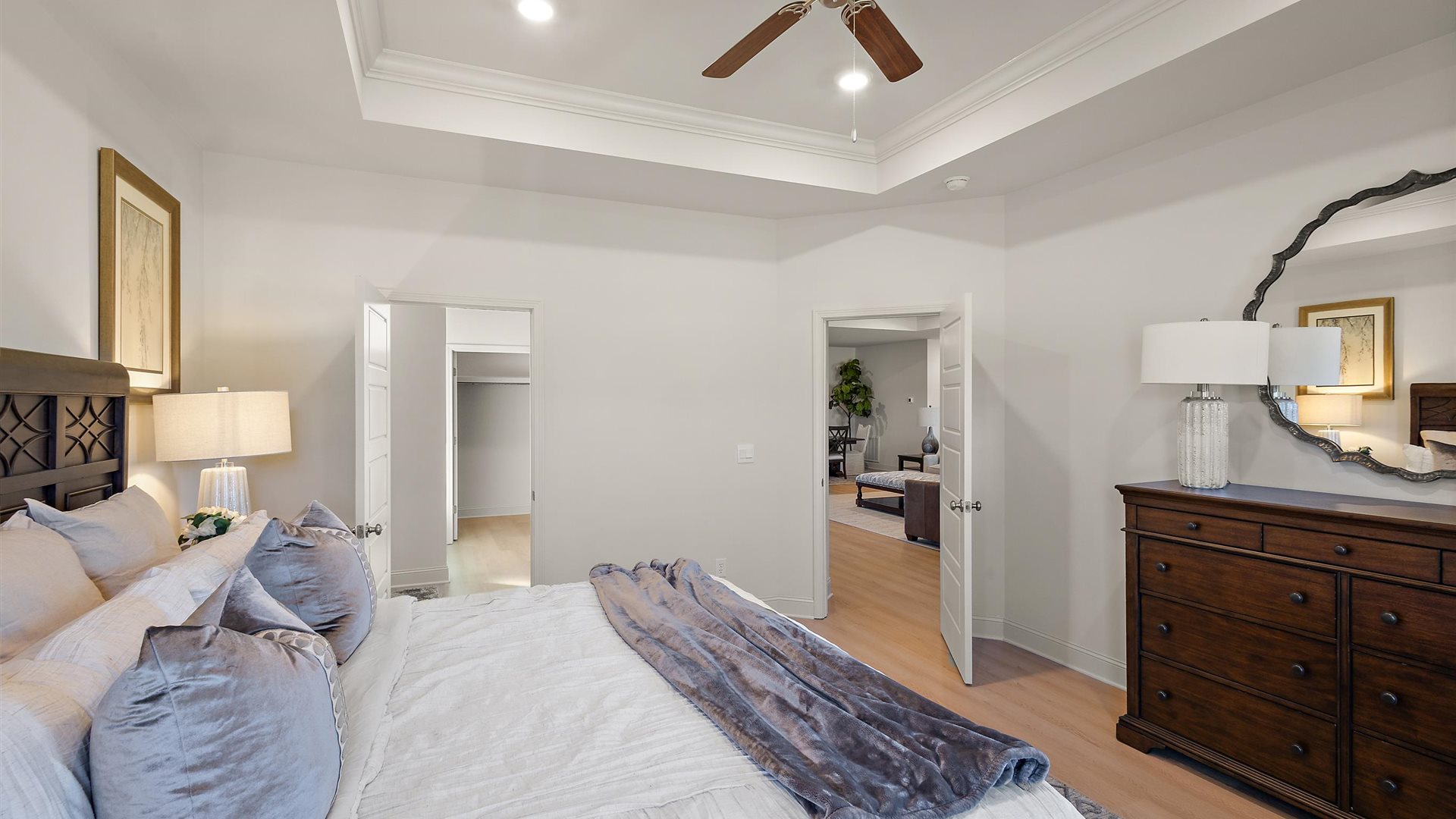 Primary bedroom with tray ceilings, hardwood floors, ceiling fan, and windows.
