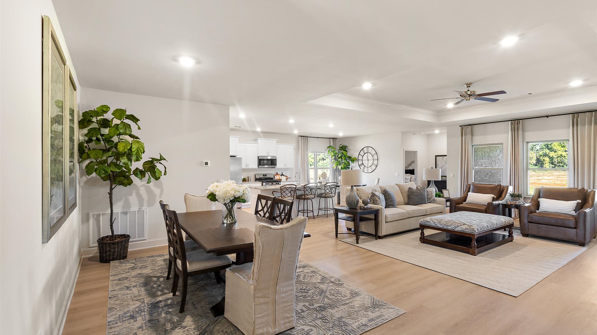 A spacious open floor plan living room, large windows, hardwood floors, and tray ceilings.