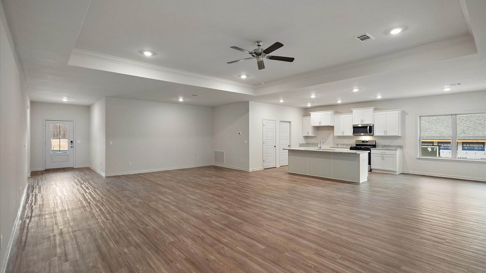 A spacious open floor plan living room, large windows, hardwood floors, and trey ceilings.