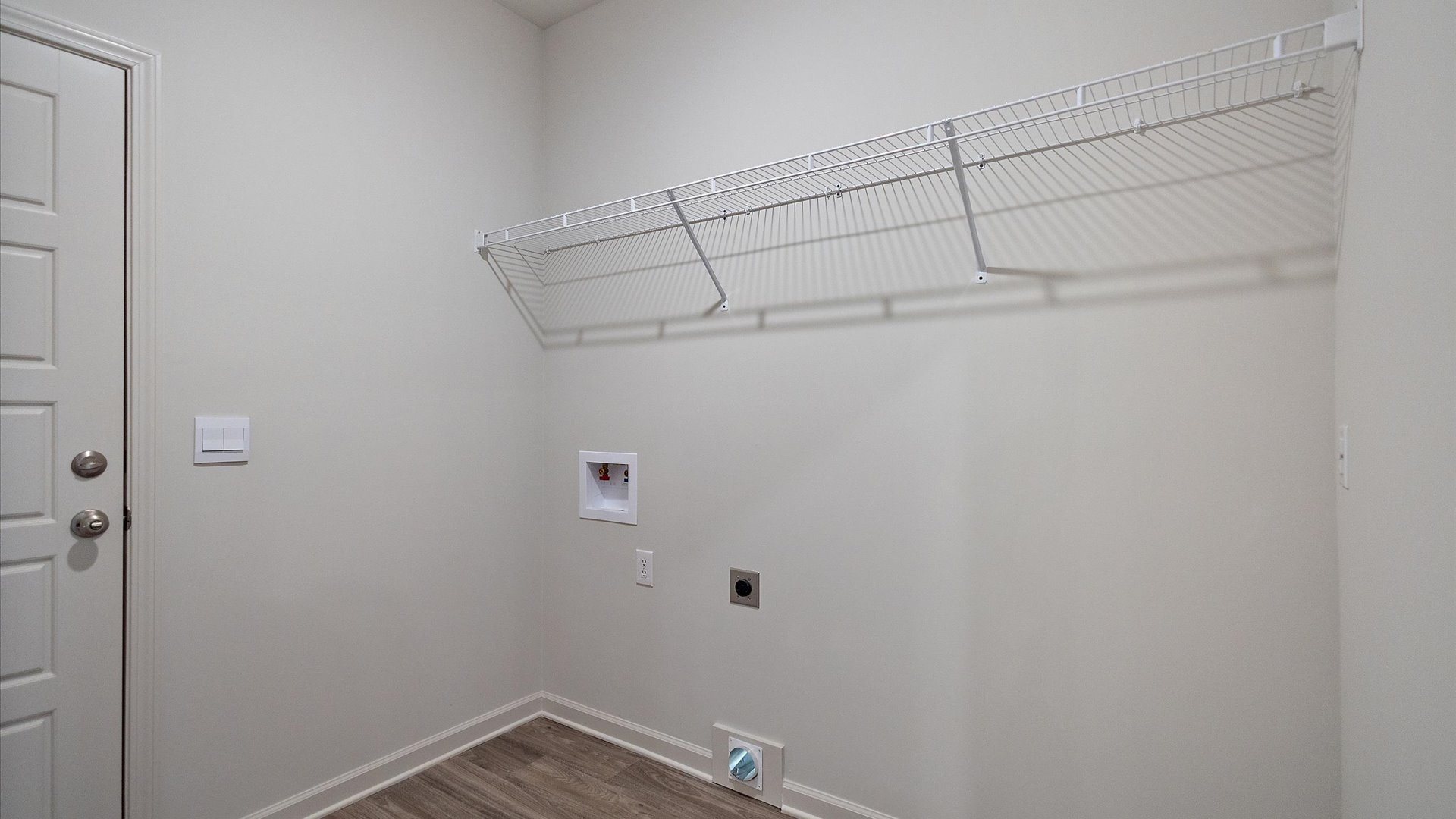 Spacious laundry area has room for a washer and dryer with mounted wire shelving.
