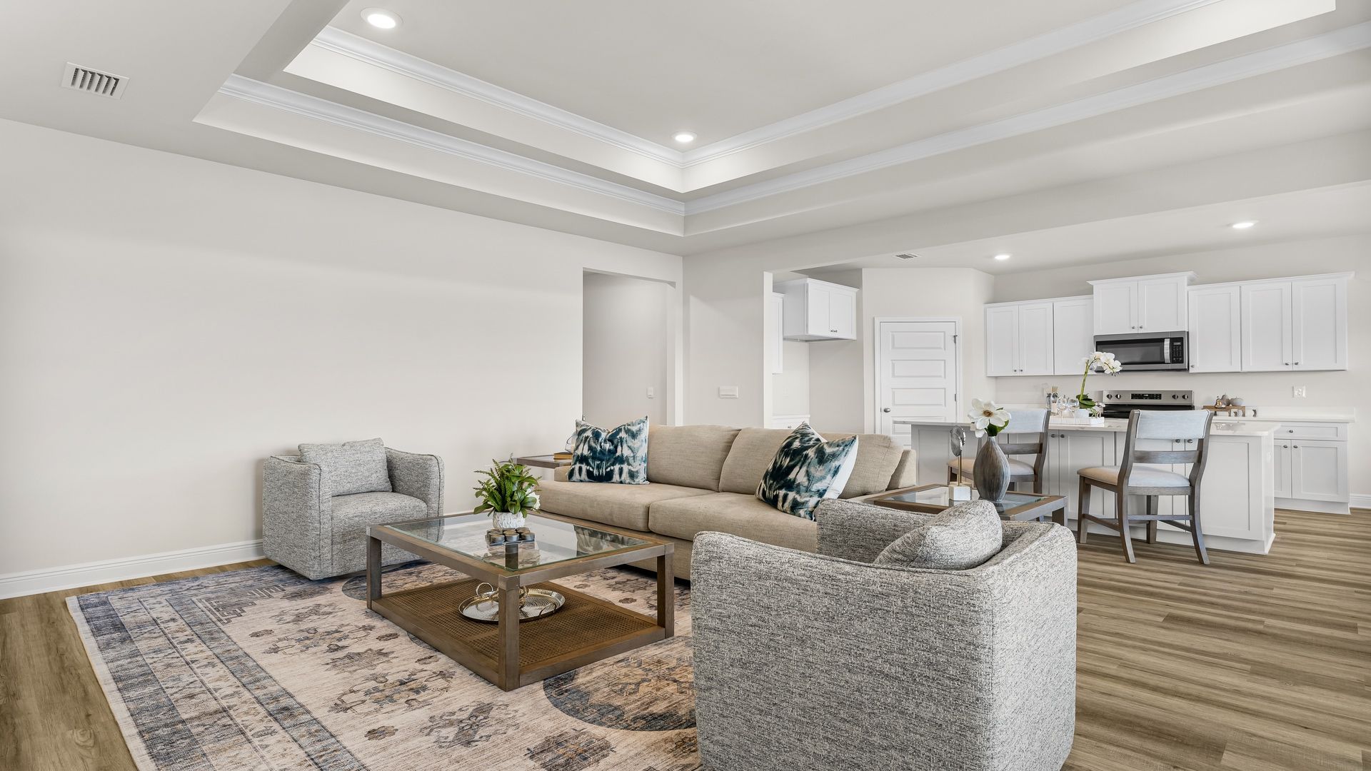 A spacious open floor plan living room, large windows, hardwood floors, and trey ceilings.