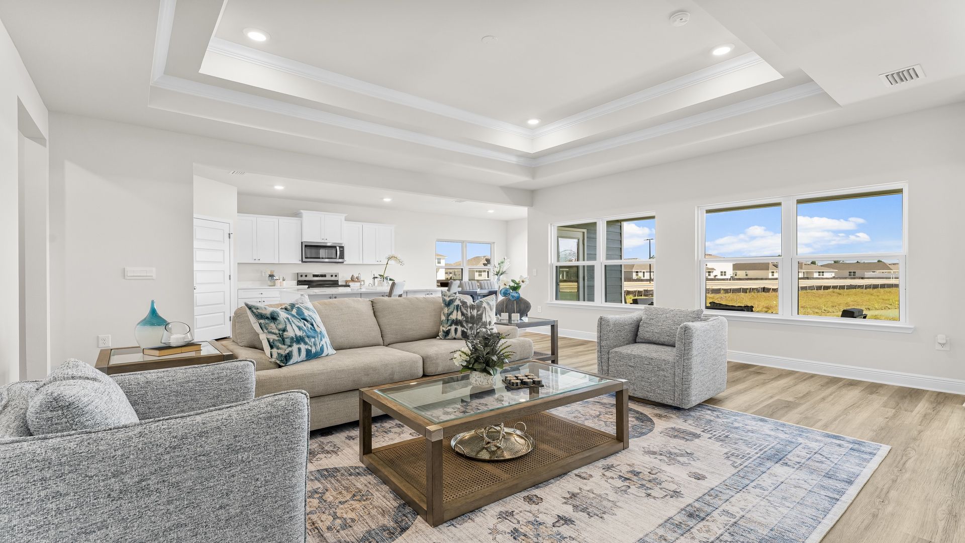 A spacious open floor plan living room, large windows, hardwood floors, and trey ceilings.