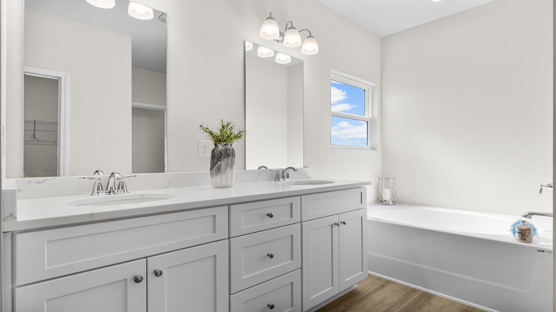 A modern bathroom featuring a double vanity with granite countertops, bright light fixtures, and a shower with adjacent tub.