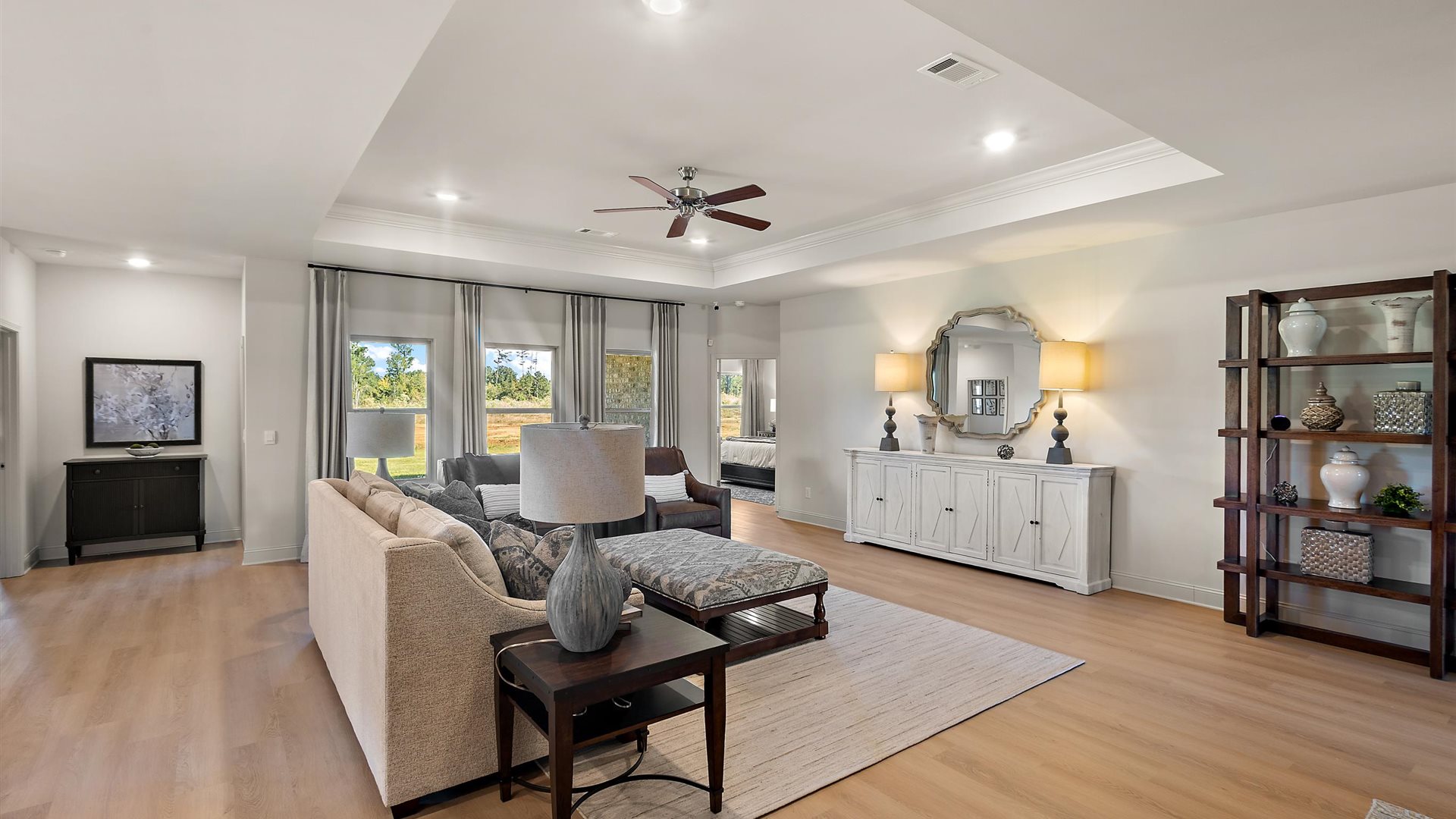 A spacious open floor plan living room, large windows, hardwood floors, and tray ceilings.