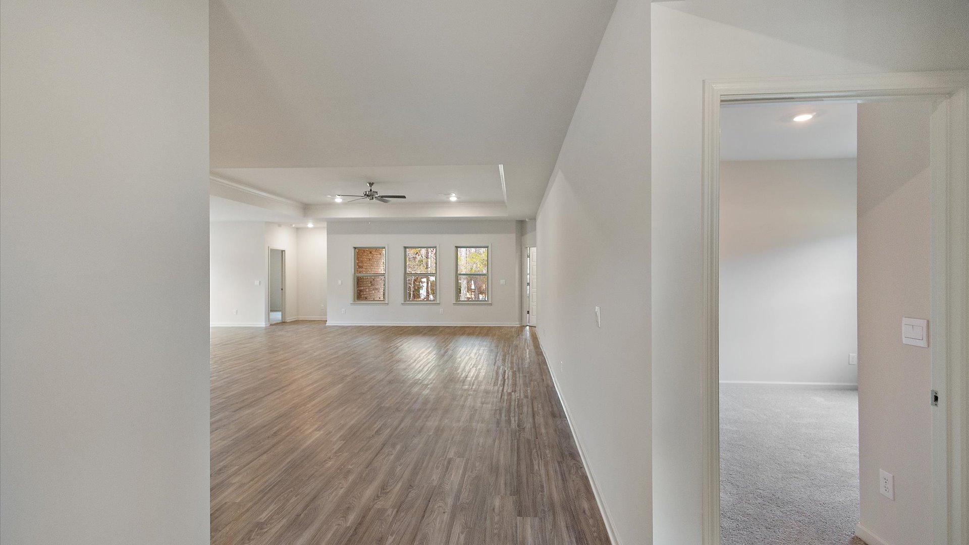 A spacious open floor plan living room, large windows, hardwood floors, and trey ceilings.