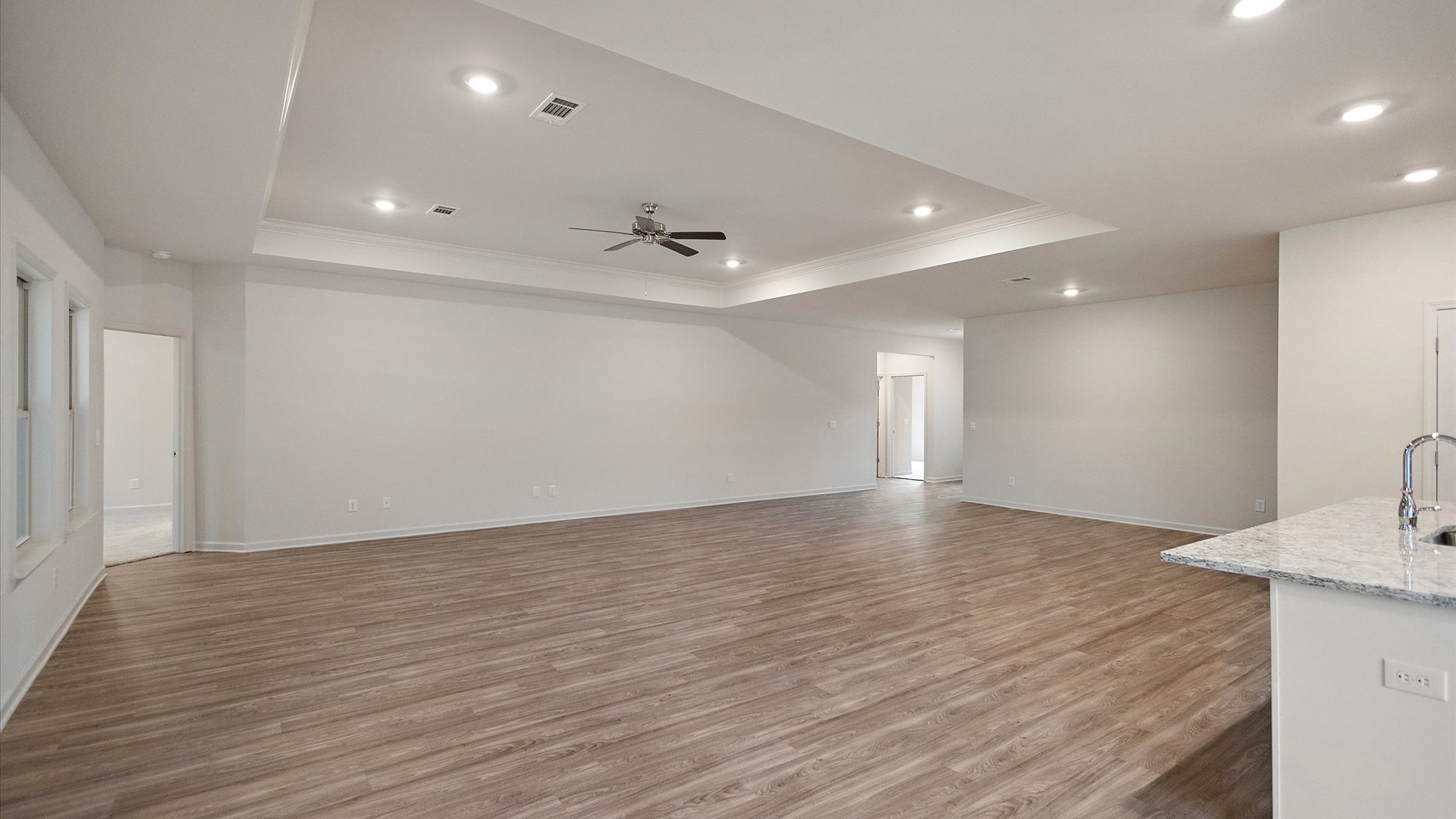 A spacious open floor plan living room, large windows, hardwood floors, and trey ceilings.