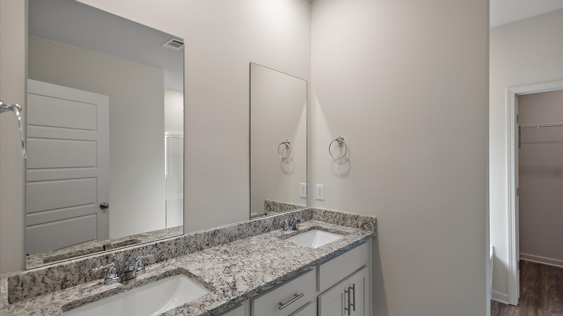 A modern bathroom featuring a double vanity with granite countertops, bright light fixtures, and a shower with adjacent tub.