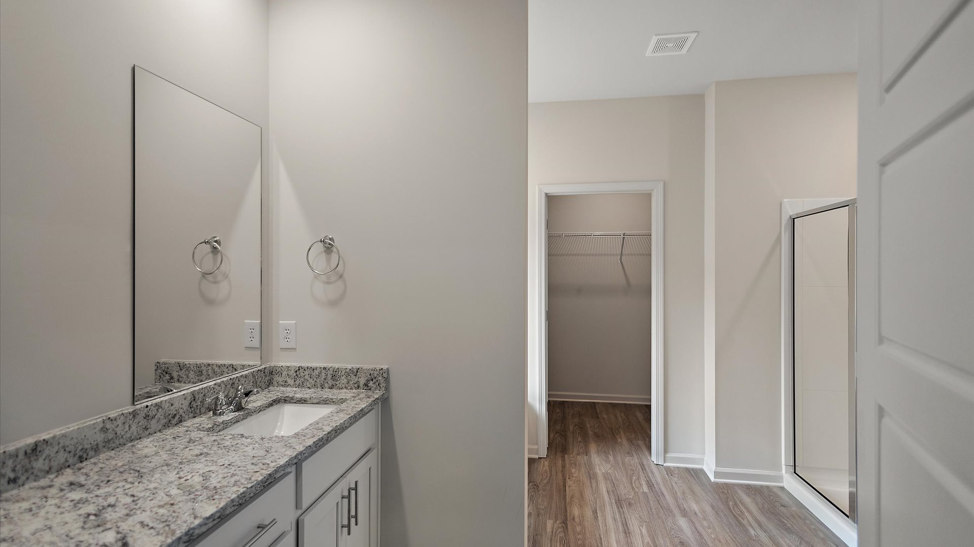 A modern bathroom featuring a double vanity with granite countertops, bright light fixtures, and a shower with adjacent tub.