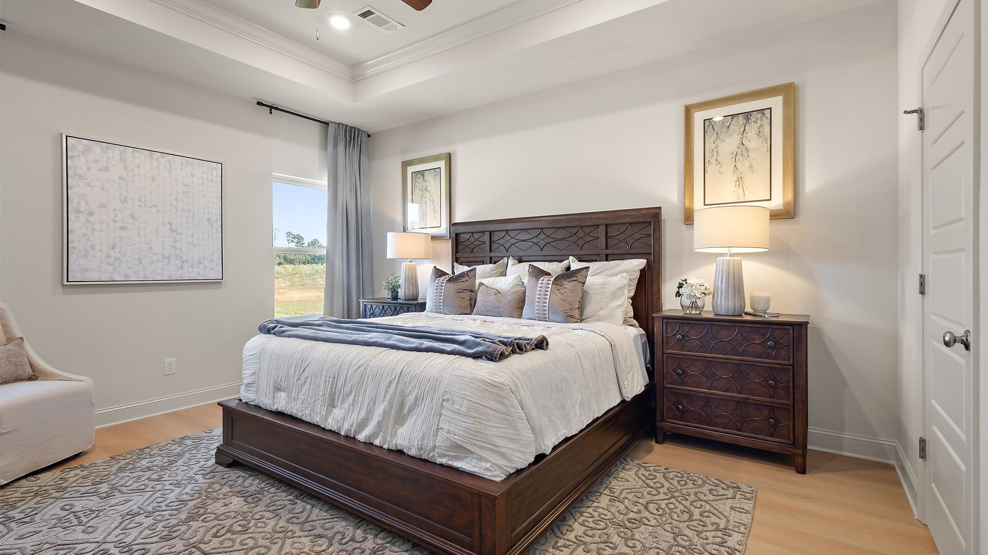 Primary bedroom with tray ceilings, hardwood floors, ceiling fan, and windows.