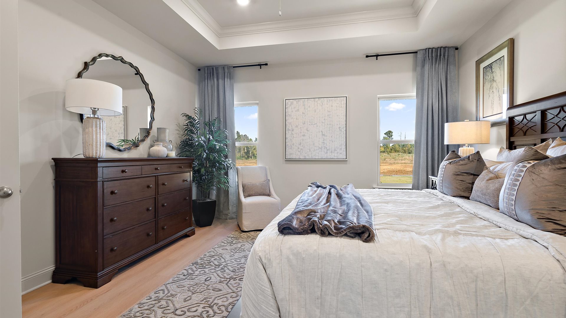 Primary bedroom with tray ceilings, hardwood floors, ceiling fan, and windows.