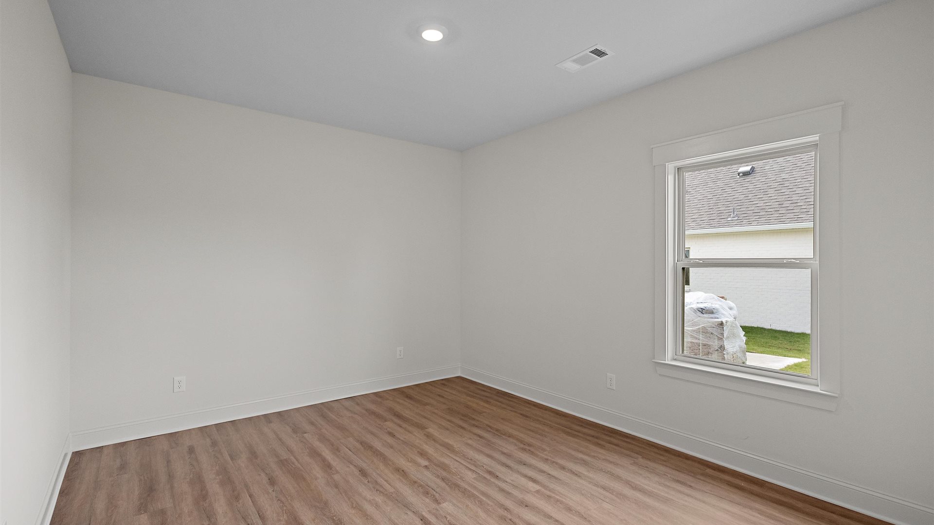 bedroom with brown flooring, and white walls, and a window on the back wall
