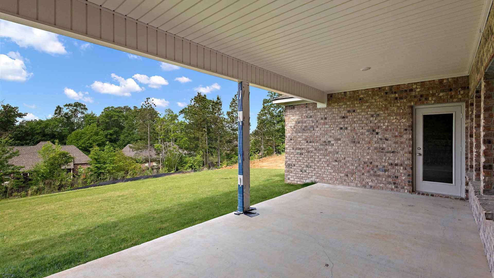 covered concrete back patio of the home with a view of a luscious backyard