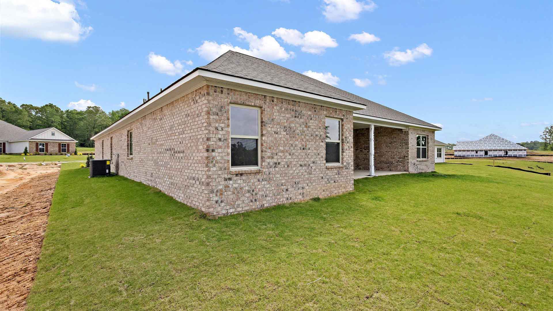 covered concrete back patio of the home with a view of a luscious backyard