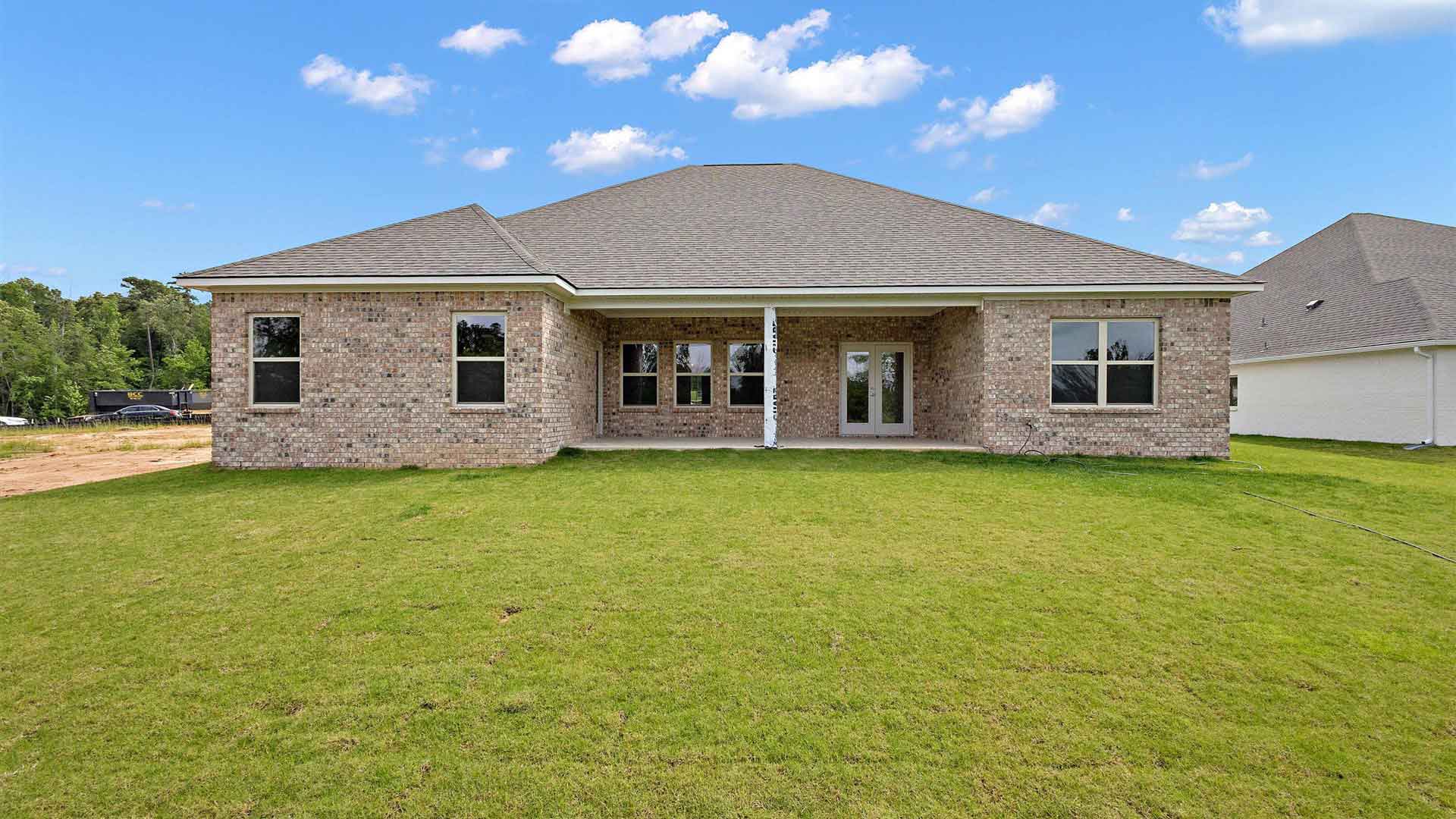 covered concrete back patio of the home with a view of a luscious backyard