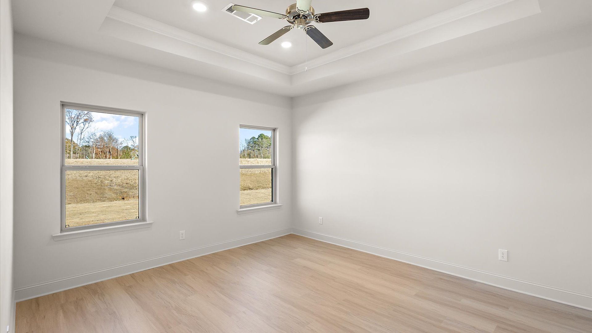 primary bedroom with hardwood floors, tray ceilings, recessed lighting, ceiling fan, and window for natural light
