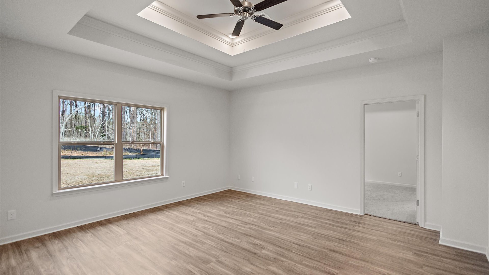 A spacious open floor plan living room, large windows, hardwood floors, and trey ceilings.