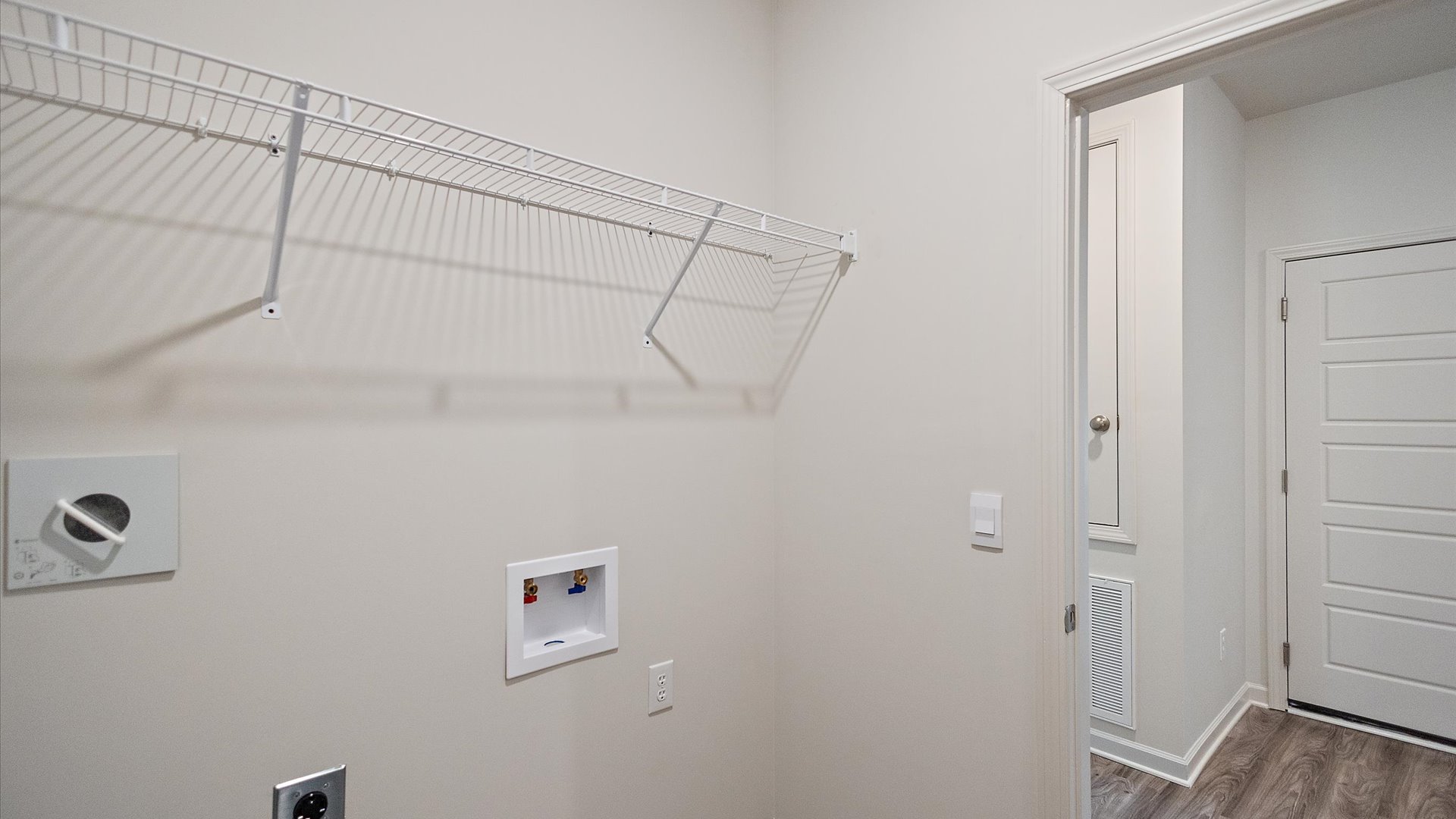 Spacious laundry area has room for a washer and dryer with mounted wire shelving.