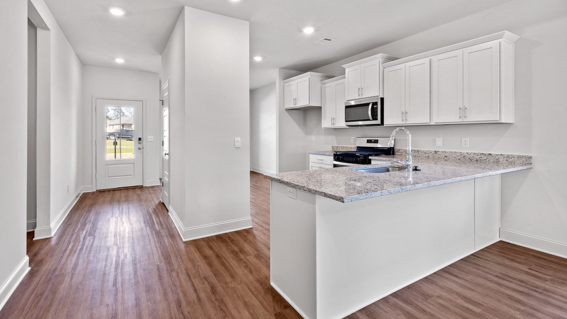 Kitchen with white shaker cabinets, granite countertops, and stainless steel appliances with a view of the front door.