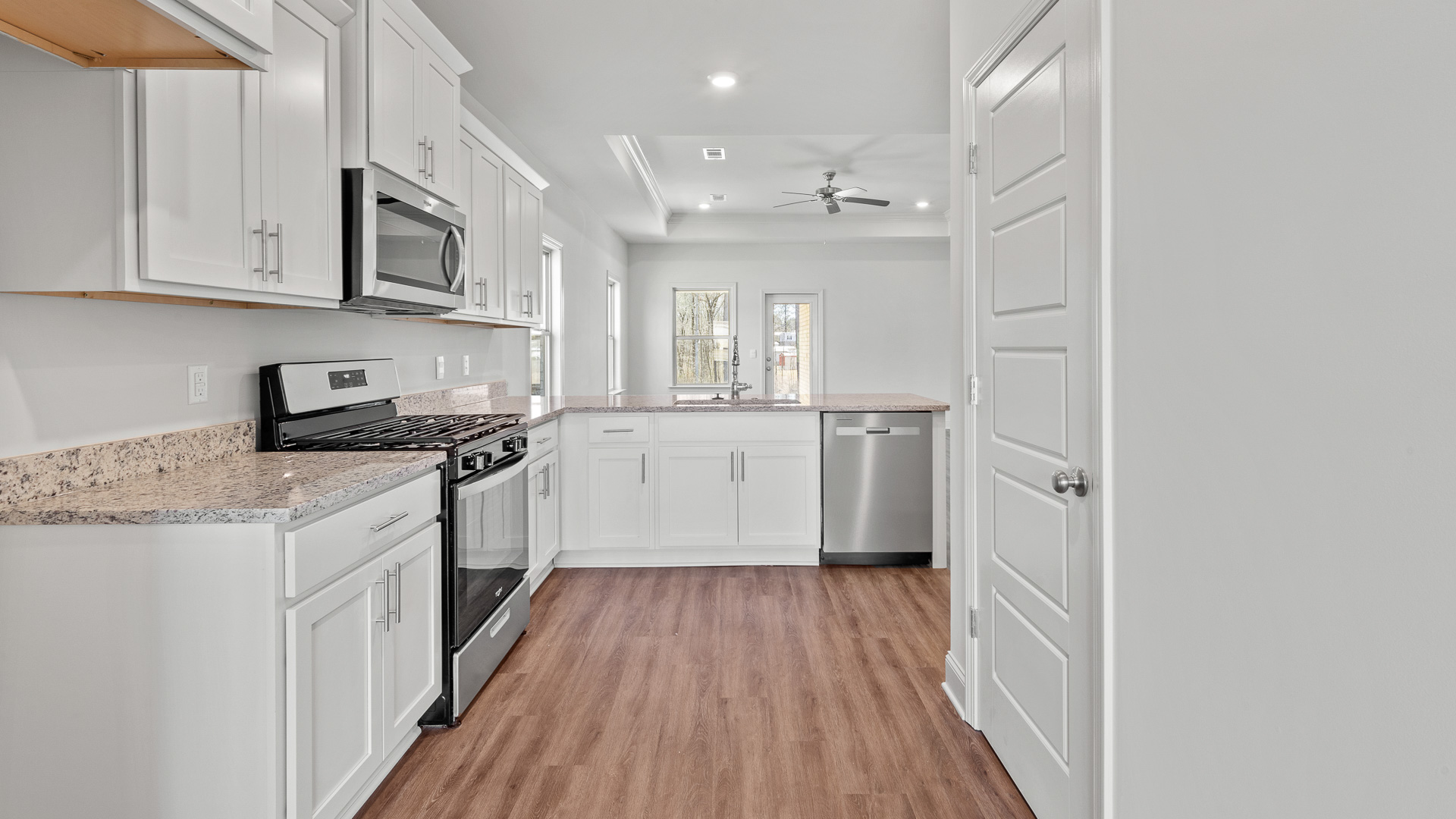 The kitchen has white shaker cabinets, granite countertops, stainless steel appliances, and the pantry door with a view of the living room, which has three single windows and a glass back door.