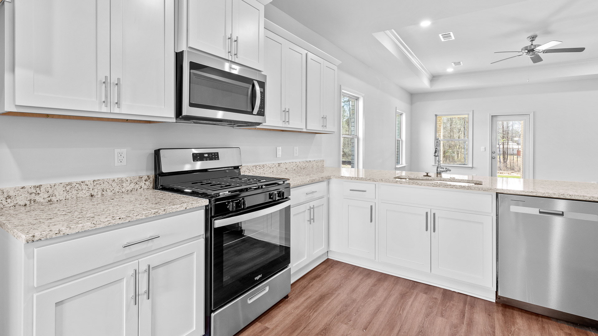 Kitchen has granite countertops, stainless steel appliances, and white shaker-style cabinets open to the living room.
