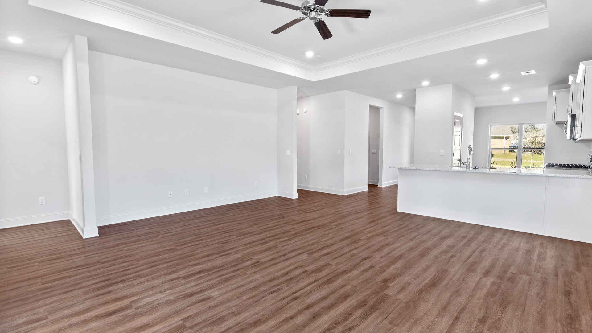 Open concept living room with a double tray ceiling, ceiling fan, canned lighting and a view of the kitchen/dining room area.
