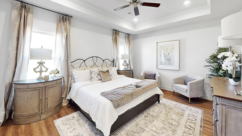 primary bedroom with hardwood floors, tray ceilings, and ceiling fans
