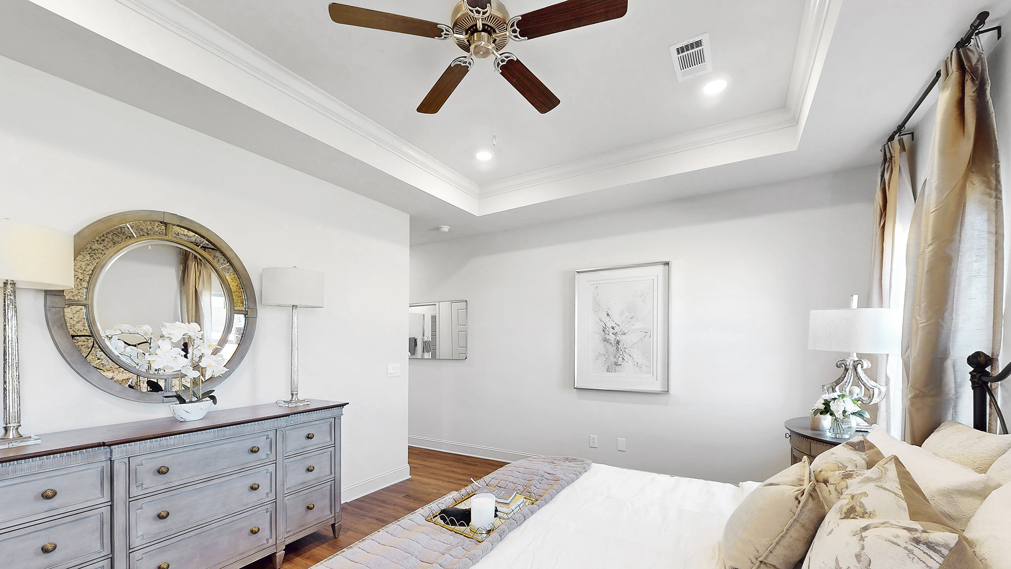 primary bedroom with hardwood floors, tray ceilings, and ceiling fans