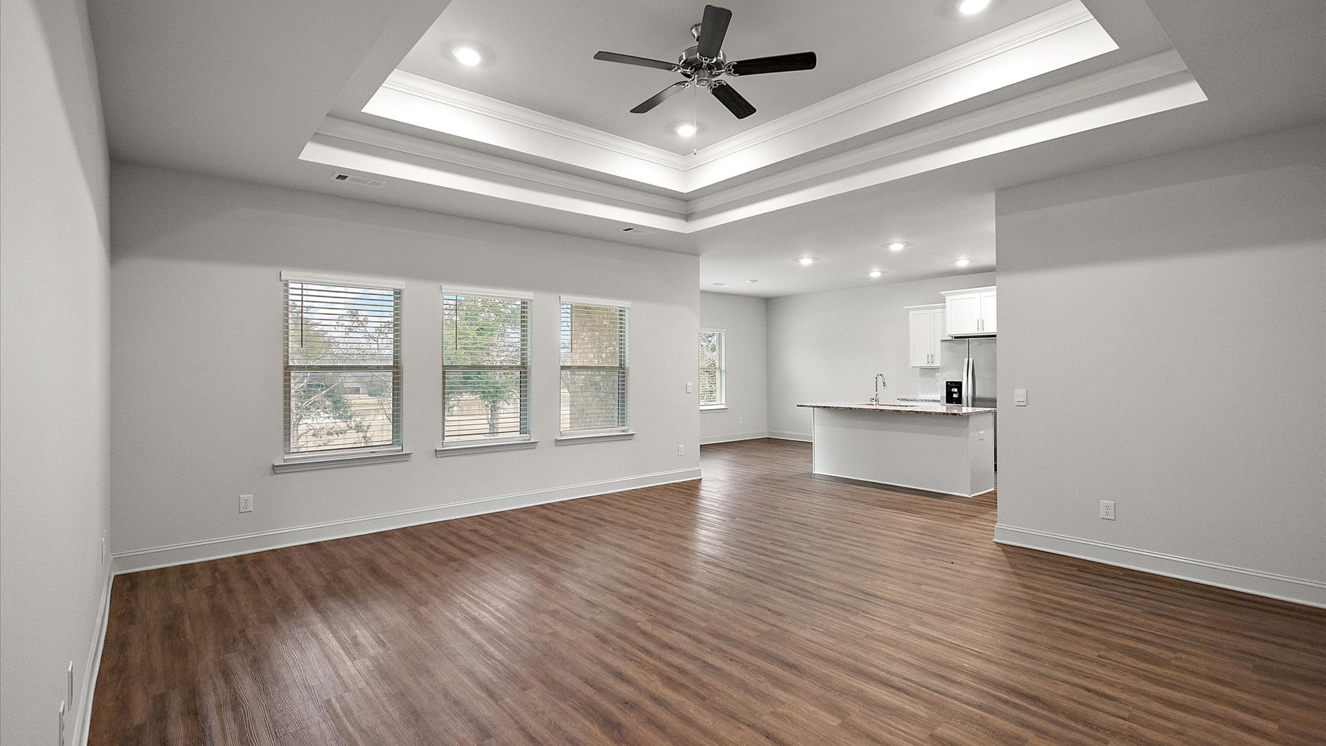 Modern open concept living room with hardwood floors, tray ceilings, ceiling fan, and large windows.