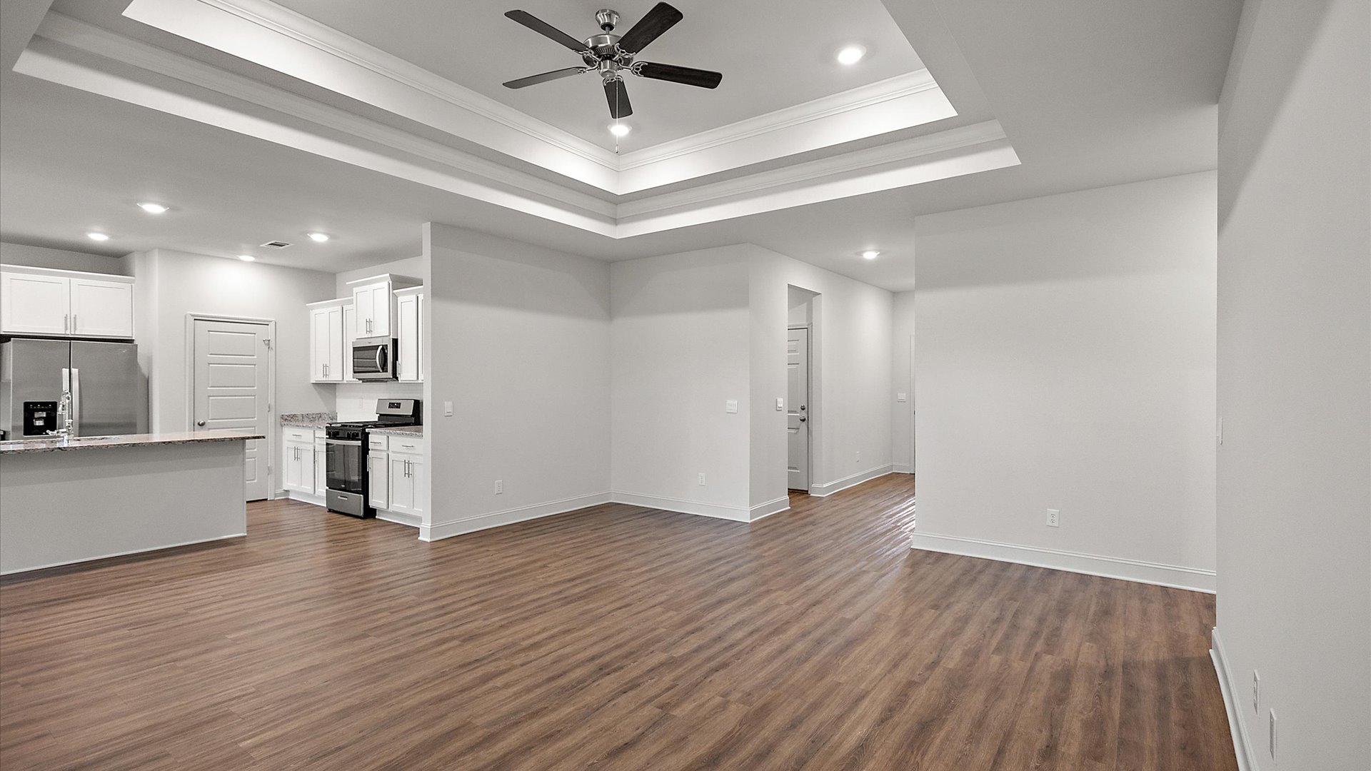 Modern open concept living room with hardwood floors, tray ceilings, ceiling fan, and large windows.