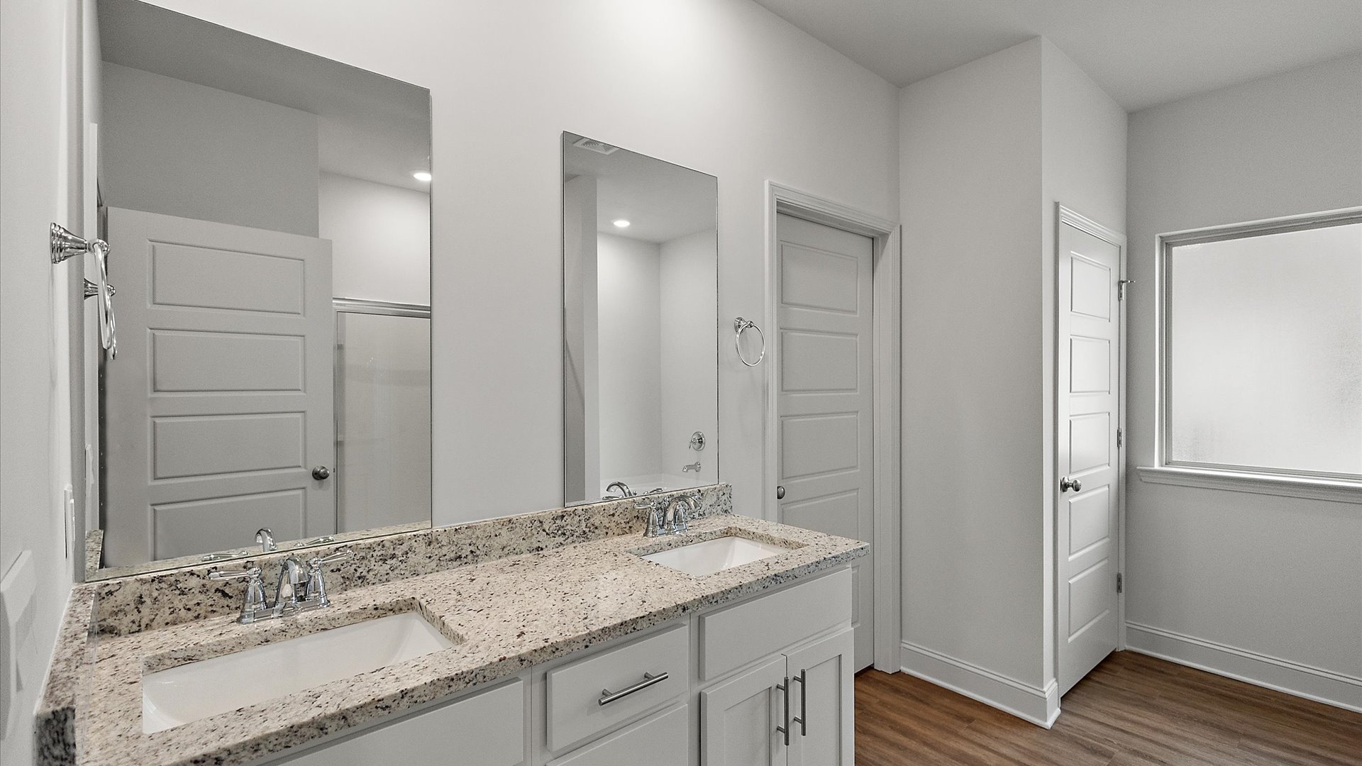Primary bathroom featuring a double vanity with granite countertops and bright light fixtures.