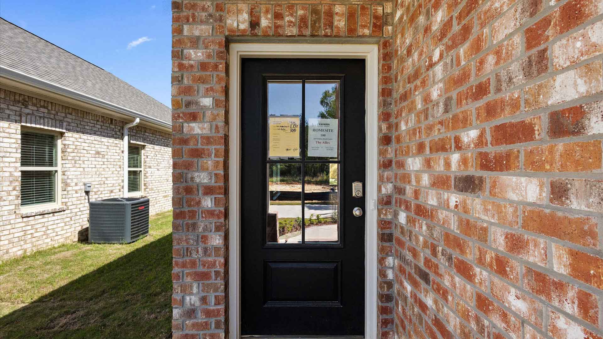 Front door with dark paint and a window surrounded buy brown brick.