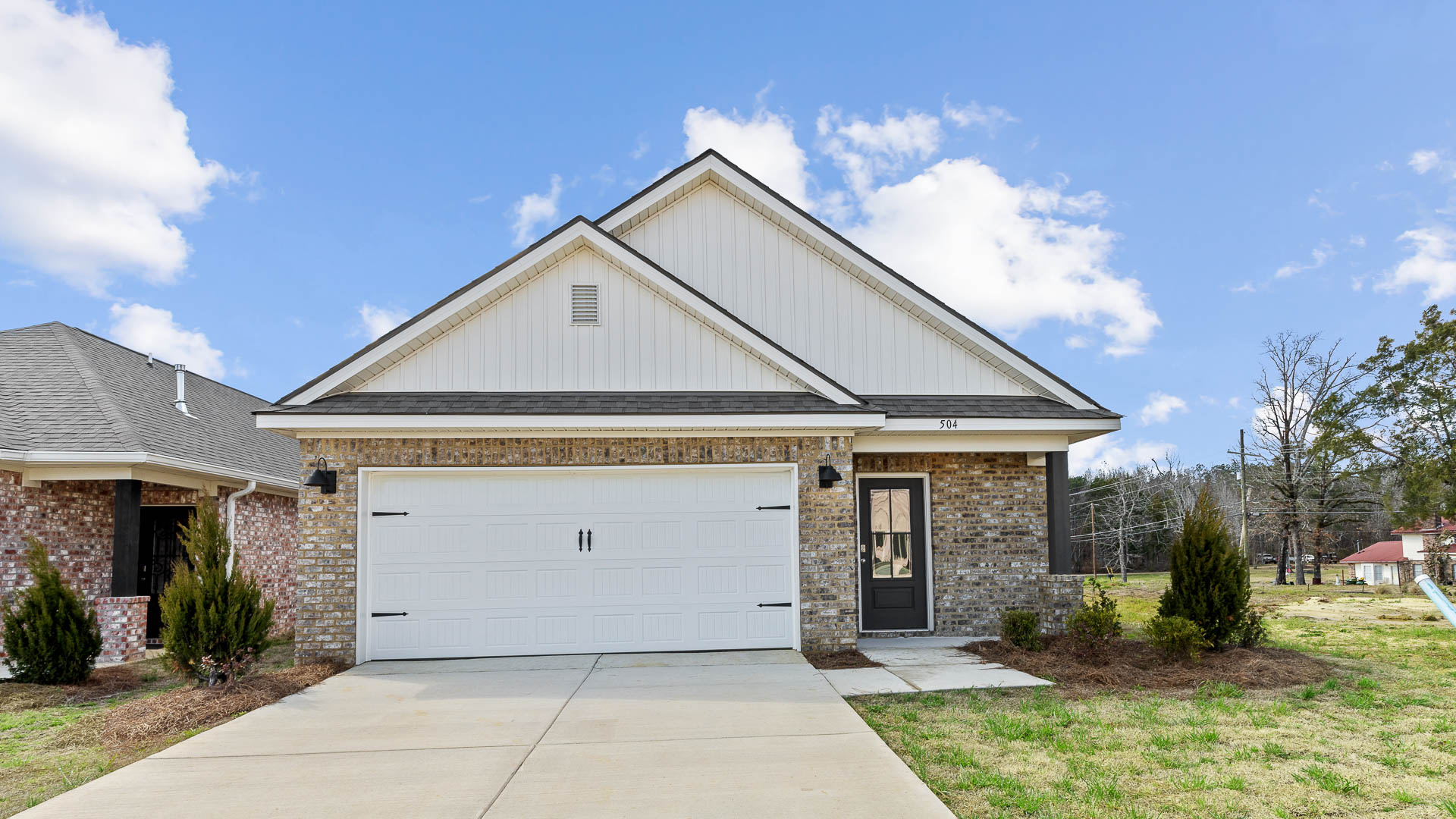 front exterior of a one story home featuring light grey siding, brick accents and a 2 car garage