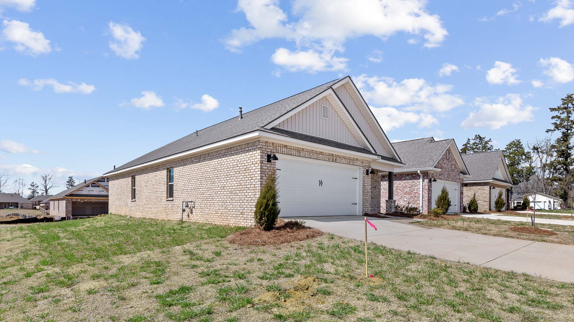front exterior of a one story home featuring light grey siding, brick accents and a 2 car garage
