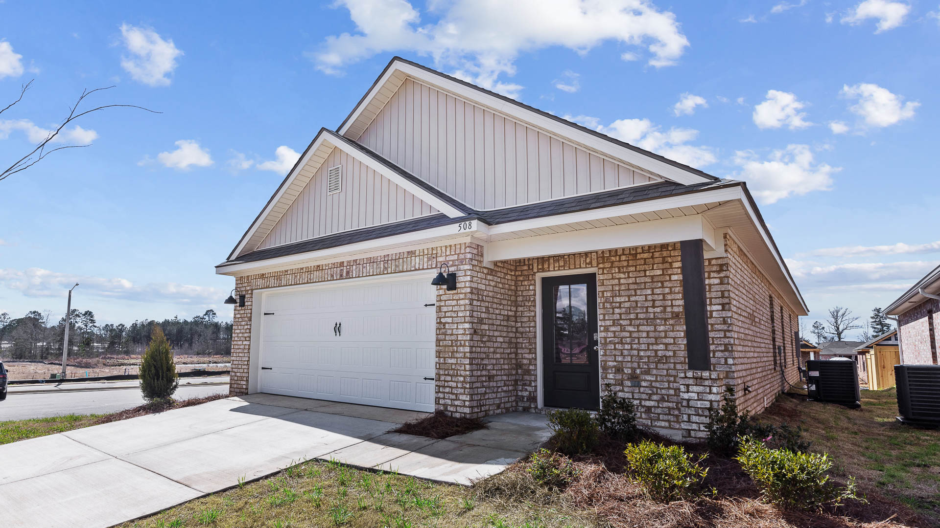 front exterior of a one story home featuring light grey siding, brick accents and a 2 car garage