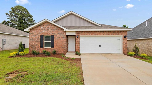 Freeport floorplan in the Foxwood community in Jackson, MS. Front exterior single story home with red/brown brick and white paneling and black shutters on the windows with side walk to the front door. The two-car garage and driveway.