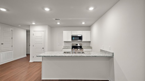 Kitchen view from behind the island with granite countertops, large island, white cabinets, and stainless steel appliances.