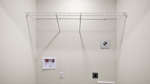 Spacious laundry area has room for a washer and dryer with mounted wire shelving.