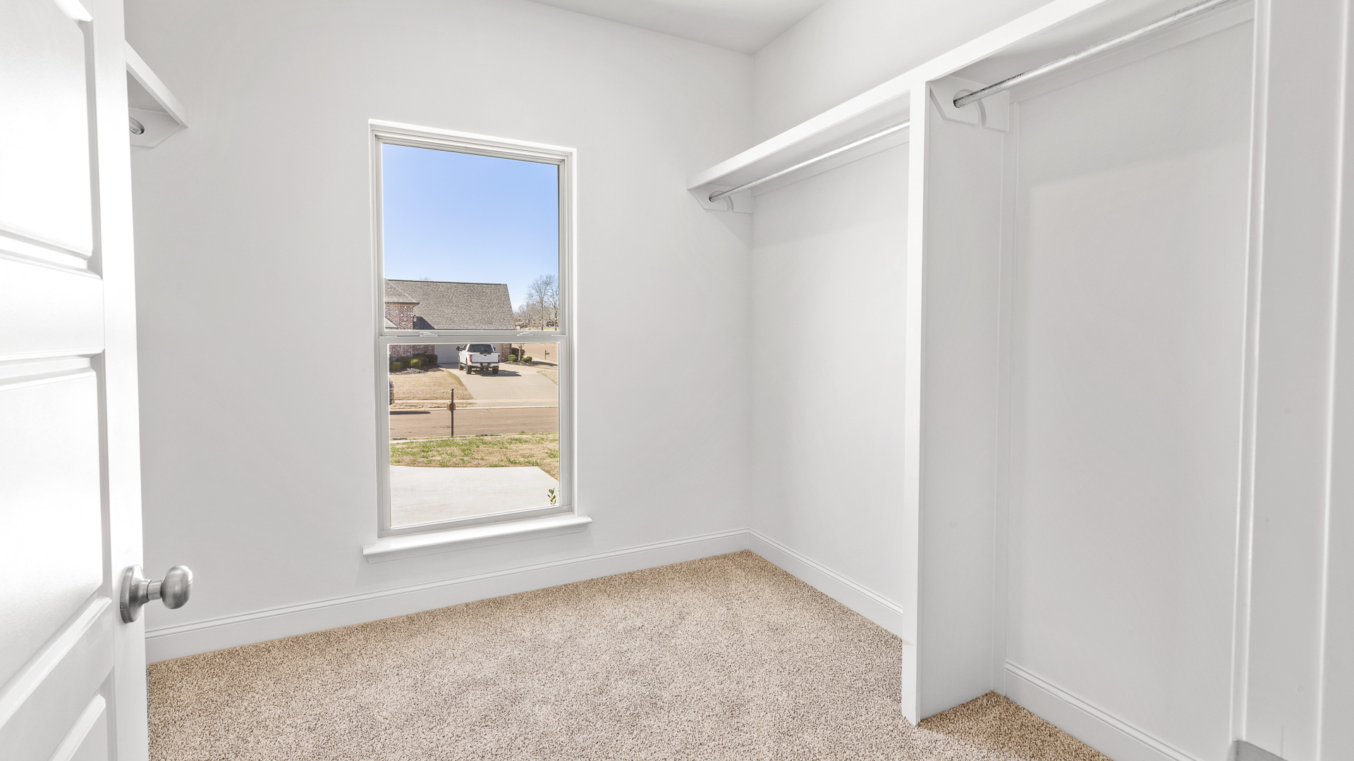 Primary walk in closet with carpeted floors and window for natural lighting.