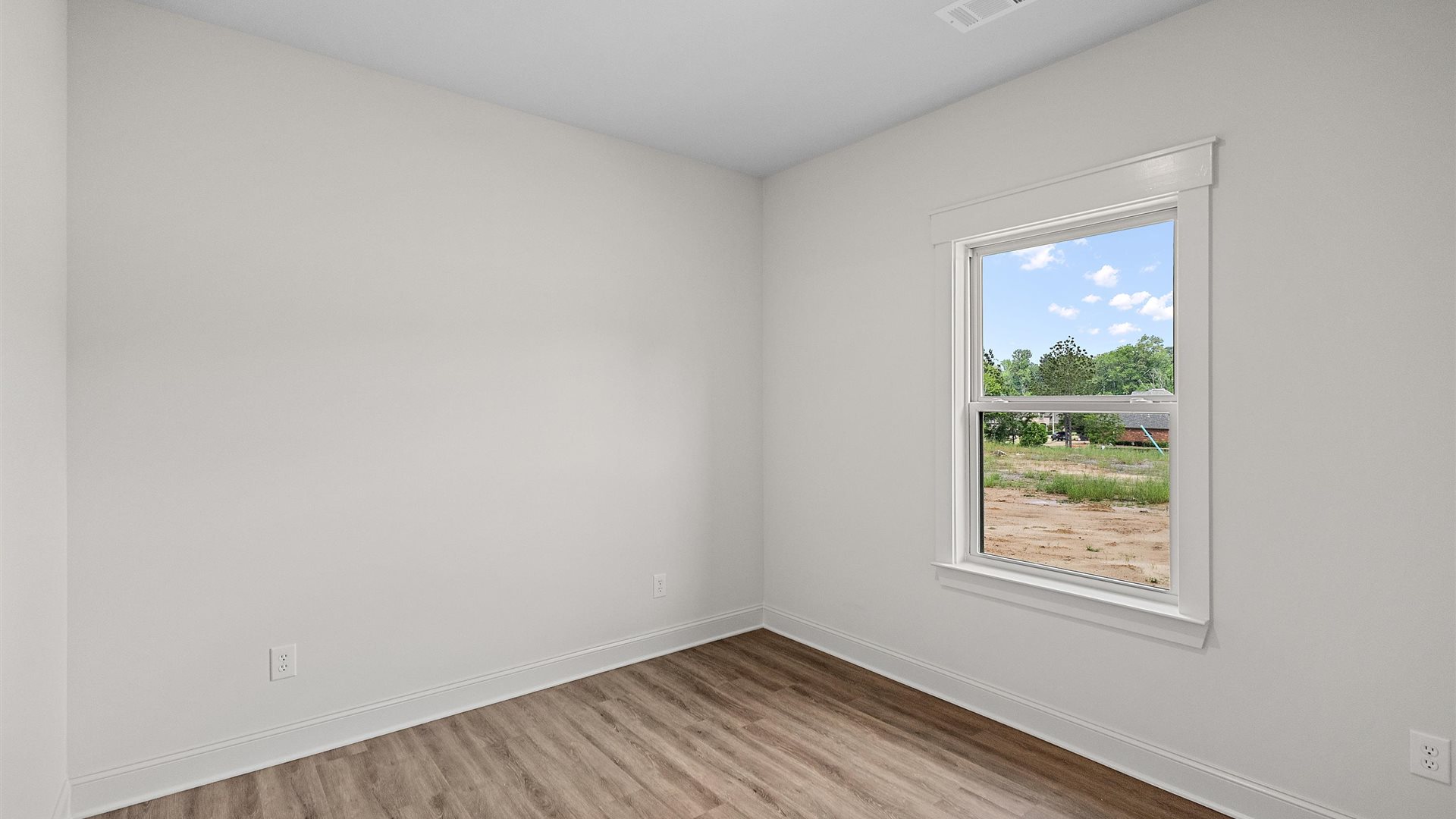 bedroom with brown flooring, and white walls, and a window on the back wall