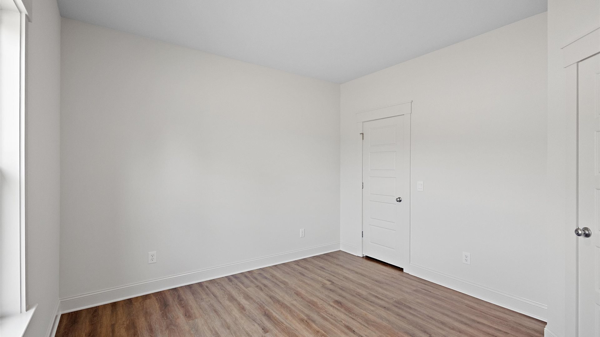 bedroom with brown flooring, white walls and a view of the doors leading to the closet, and hallway